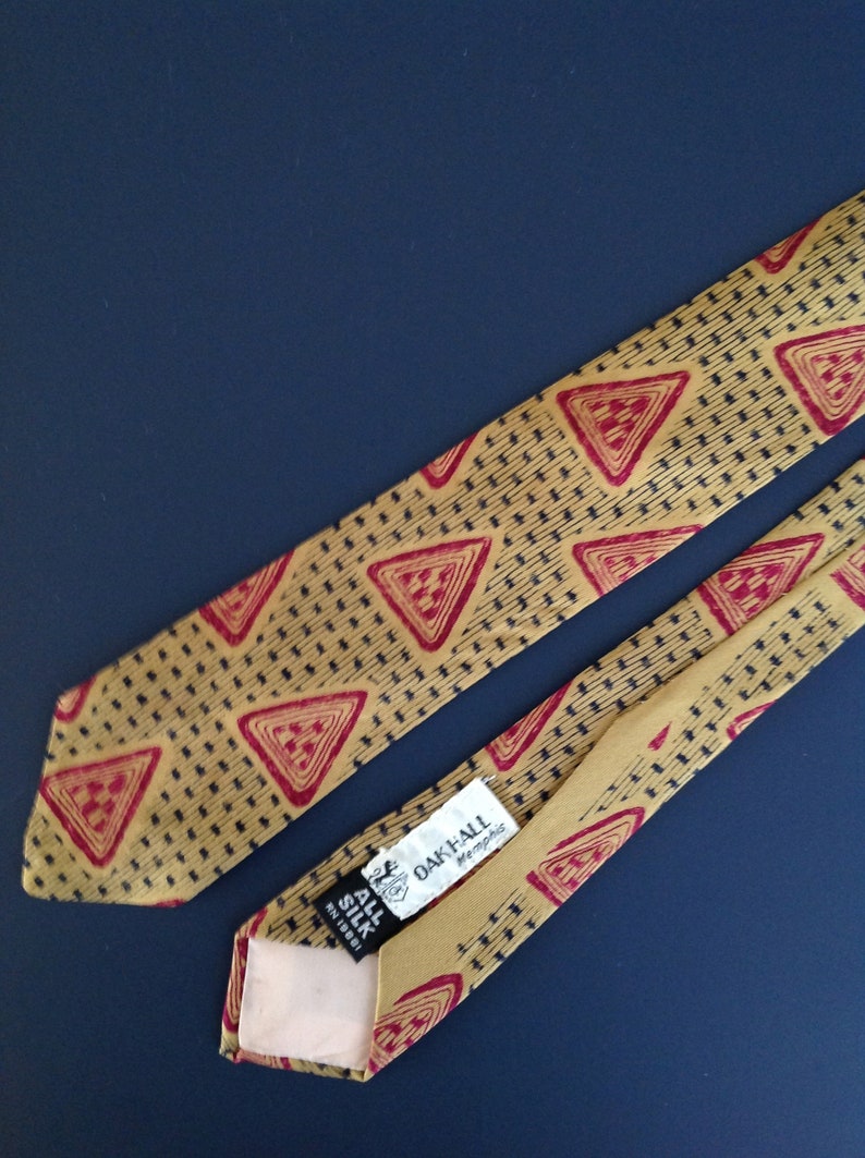 May include: A gold silk tie with a red and black geometric pattern. The tie has a label that reads "Oak-All Memphis" and "All Silk Reg. 10001".