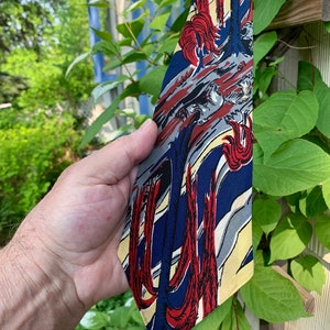 May include: A blue, red, and yellow patterned tie with a stylized design of trees and birds.
