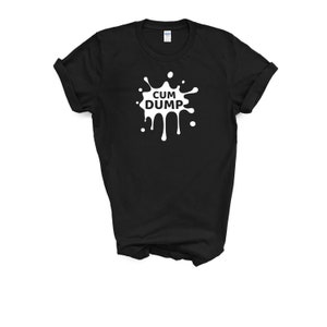 May include: Black t-shirt with a white graphic that reads "CUM DUMP" in a stylized font. The graphic is designed to resemble a splash or splatter. The shirt is made of a soft material and has a crew neck.