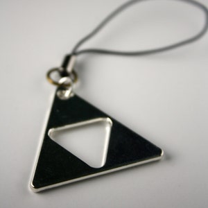 Pode incluir: Um chaveiro de triângulo prateado com um triângulo menor cortado no centro. O chaveiro está preso a um cordão preto.