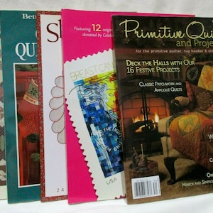 Könnte beinhalten: Vier Quiltbücher mit bunten Umschlägen. Das erste Buch ist braun mit einem Quiltmuster auf dem Umschlag. Das zweite Buch ist türkis mit dem Wort "Quilts" auf dem Umschlag. Das dritte Buch ist pink mit den Worten "Breast Cancer" auf dem Umschlag. Das vierte Buch ist eine Zeitschrift mit den Worten "Primitive Quilts and Projects" auf dem Umschlag.