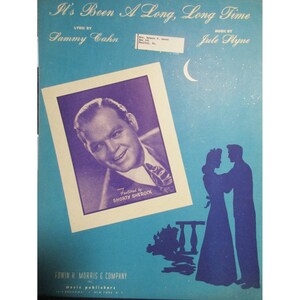 May include: A vintage sheet music cover with a blue background. The title "It's Been A Long, Long Time" is printed in black. The lyrics are by Sammy Cahn and the music is by Jule Styne. A black and white photo of a man is in the upper left corner. A silhouette of a couple dancing is in the lower right corner.