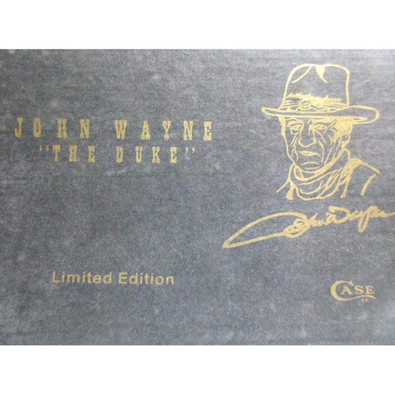 May include: A dark gray rectangular box featuring gold text that reads JOHN WAYNE THE DUKE, a gold line drawing of John Wayne wearing a cowboy hat, a gold signature, the text Limited Edition, and a small gold Case logo in the bottom corner.