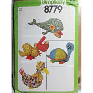Puede incluir: Un sobre de patrón de costura Simplicity 8779 con ilustraciones de cuatro animales de peluche: una ballena floral, un pájaro amarillo y rojo, una gallina de patchwork con capota y una tortuga multicolor. El paquete está etiquetado como One Size.