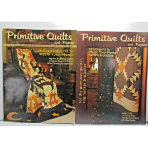 May include: Two magazines titled "Primitive Quilts and Projects" are displayed. The left magazine cover features a quilt with orange stars and a black border. The right magazine cover shows a quilt with star and triangle patterns. Text includes "15 Cozy Projects" and "16 Projects to Warm Your Home."