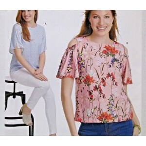 May include: Two women's tops are shown. One is a light blue top with short sleeves and a subtle pattern. The other is a pink top with a floral print, featuring cold shoulder sleeves. Both tops are stylish and suitable for various occasions.