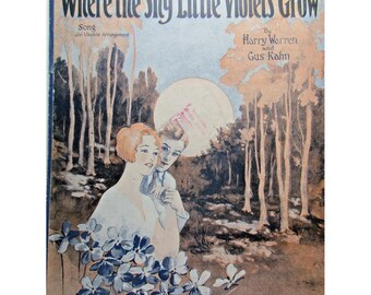 May include: Vintage sheet music cover titled "Where the Shy Little Violets Grow." The artwork features a couple, a woman with red hair and a man, with a backdrop of trees and a large sun. Blue violets are in the foreground. The song is by Harry Warren and Gus Kahn.