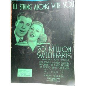 May include: A vintage sheet music cover titled I'll String Along With You from 20 Million Sweethearts. The black and green graphic features portraits of Dick Powell and Ginger Rogers, with credits for Al Dubin, Harry Warren, and M. Witmark & Sons.