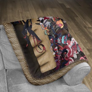 以下が含まれることがあります： 詳細なイラストが施された、柔らかいブランケット。 赤いアクセントの暗い人物と、カラフルなキャラクターのコラージュが特徴です。 ブランケットは茶色の縁取りがあり、灰色のソファに掛けられています。