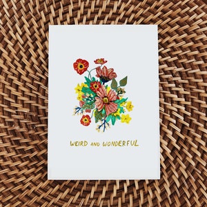May include: A white card with a colorful floral illustration and the text "Weird and Wonderful" in gold lettering.