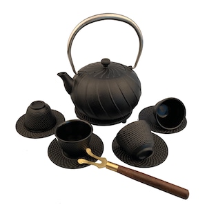 May include: Black cast iron teapot with a silver handle and four matching cups and saucers. The teapot has a ribbed design and a small spout. The cups and saucers have a textured surface. A brass tea tong is included.