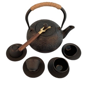 May include: A black cast iron teapot with a wooden handle and a matching set of four teacups and saucers. The teapot has a textured surface and a gold-colored lid.