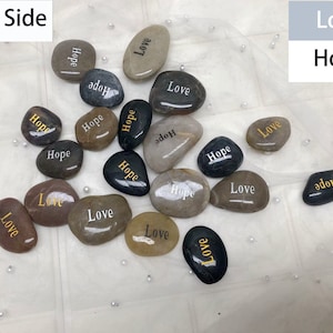 May include: A collection of smooth, gray and brown stones with the words "Love" and "Hope" inscribed in gold lettering.