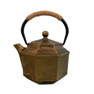 May include: A gold cast iron teapot with a rustic finish and a rope handle. The teapot has an octagonal shape and a small knob on the lid.