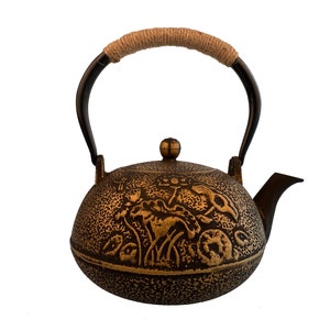 May include: A black cast iron teapot with a gold floral design and a rope handle.