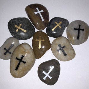 May include: A collection of ten smooth, round stones with painted crosses. Some crosses are gold, some are black, and some are white.