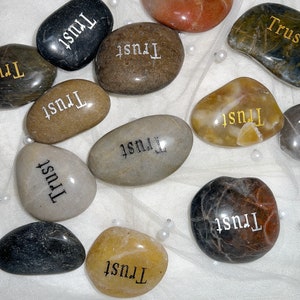 May include: A collection of smooth, gray, brown, and white stones with the word "Trust" inscribed on each one.