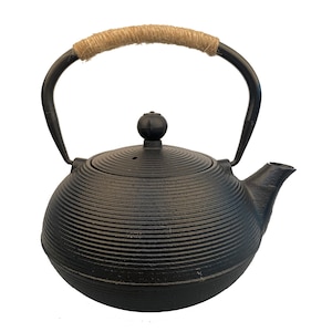 May include: Black cast iron teapot with a rope handle and a ribbed design. The teapot has a round body and a small spout.