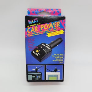 May include: A black car power adapter with the text "NAKI CAR POWER" on it. The adapter is packaged in a box with pink and white polka dots. The box also includes text that says "The Gamers Edge" and "Works with any hand held electronic video game".