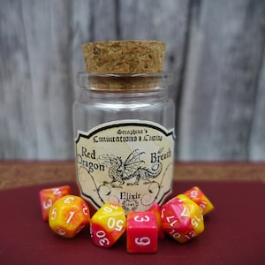 Könnte beinhalten: Eine kleine Glasflasche mit einem Korkverschluss und einem Etikett mit der Aufschrift "Seraphina's Coniurations & Curios Red Dragon Breath Elixir". Die Flasche ist von sechs roten und gelben Würfeln mit weißen Zahlen umgeben.