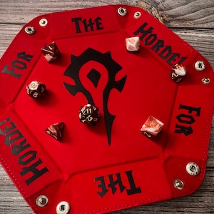 Può includere: Vassoio da gioco in feltro rosso con un simbolo dell'Orda nero e il testo "Per l'Orda!" stampato sui lati. Il vassoio è rivestito in feltro nero ed è progettato per contenere i dadi.