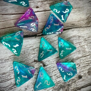 K&ouml;nnte beinhalten: Ein Satz von zehn t&uuml;rkisfarbenen und violetten, schillernden W&uuml;rfeln mit silbernen Zahlen. Die W&uuml;rfel sind in Form von dreieckigen Pyramiden.