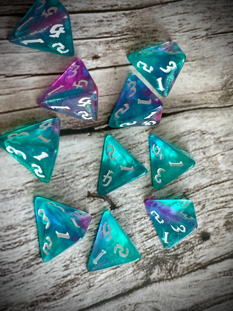 K&ouml;nnte beinhalten: Ein Satz von zehn t&uuml;rkisfarbenen und violetten, schillernden W&uuml;rfeln mit silbernen Zahlen. Die W&uuml;rfel sind in Form von dreieckigen Pyramiden.