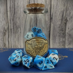 Puede incluir: Un frasco de vidrio con tapa de corcho lleno de dados de espiral azul y blanco. El frasco tiene una etiqueta que dice "Cloud Giant" y "Strength Potion".