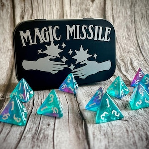 Puede incluir: Una lata de metal negra con las palabras "Magic Missile" impresas en ella. La lata está abierta y contiene ocho dados de cuatro caras iridiscentes azules y morados.