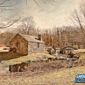 May include: A rustic stone building with a wooden bridge over a small stream. The building has a gabled roof and a chimney. The stream is surrounded by trees and foliage. The image has a vintage, faded look.
