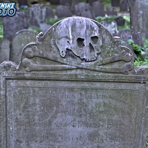 Puede incluir: Una l&aacute;pida gris y desgastada con una calavera y huesos cruzados tallados en la parte superior. La inscripci&oacute;n dice "Aqu&iacute; yace enterrado el cuerpo de BENJAMIN PARKER que parti&oacute; de esta vida".