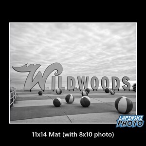 May include: Black and white photo of a sign that reads "Wildwoods" with beach balls scattered in front of it.