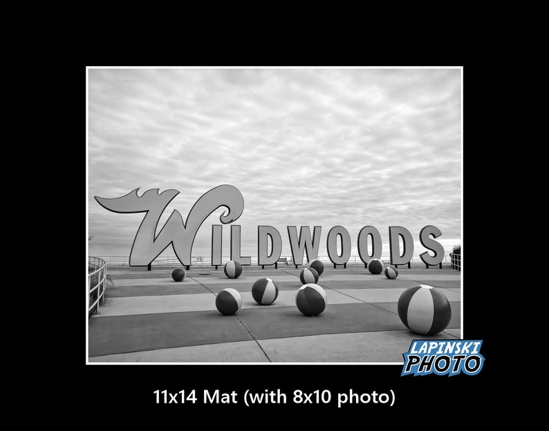 May include: Black and white photo of a sign that reads "Wildwoods" with beach balls scattered in front of it.