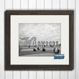 May include: Black and white photograph of the iconic "Wildwoods" sign with beach balls in the foreground. The sign is a large, stylized white letter "W" with the word "Wildwoods" in white letters on a red background.