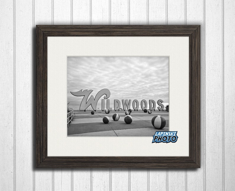 May include: Black and white photograph of the iconic "Wildwoods" sign with beach balls in the foreground. The sign is a large, stylized white letter "W" with the word "Wildwoods" in white letters on a red background.