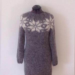 May include: A gray knitted sweater dress with long sleeves and a round neckline. The upper chest features a white snowflake design. The dress is displayed on a dress form against a white background. The text "FruStrik" is at the bottom.