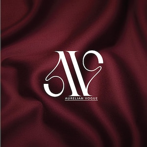 May include: White logo with the text "AURELIAN VOGUE" on a deep burgundy fabric background. The logo features stylized letters, with the "A" and "V" intertwined. The fabric has a silky, flowing texture.