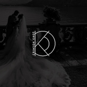 May include: Black and white image featuring a couple embracing near a body of water. A logo with the text "CRIMSON KNOT" is overlaid on the image. The logo is a stylized design with a half-circle and intersecting lines, suggesting a wedding or event theme.