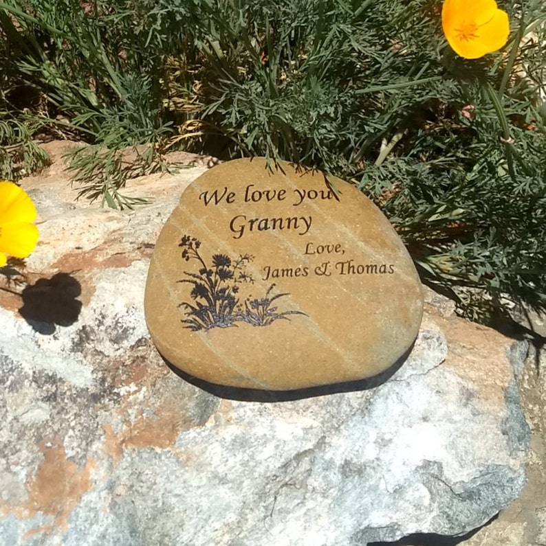 May include: A brown stone with the words "We love you Granny Love, James & Thomas" engraved on it. The stone has a black silhouette of flowers and leaves.