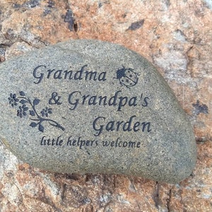 May include: A gray stone with the words "Grandma & Grandpa's Garden little helpers welcome" engraved on it. A small ladybug is also engraved on the stone.