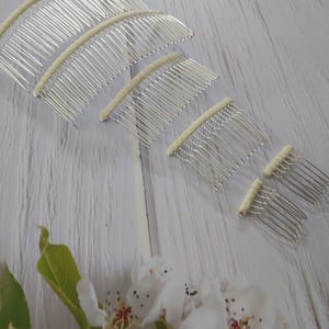 May include: A set of five silver-toned metal hair combs arranged in a descending size order. Each comb features a curved top bar wrapped in a cream-colored fabric material. The teeth of the combs are thin, metallic, and spaced evenly apart.
