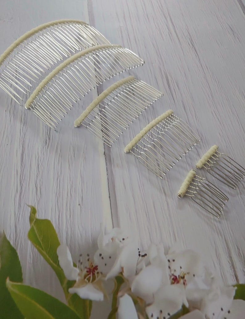 May include: A set of five silver-toned metal hair combs arranged in a descending size order. Each comb features a curved top bar wrapped in a cream-colored fabric material. The teeth of the combs are thin, metallic, and spaced evenly apart.