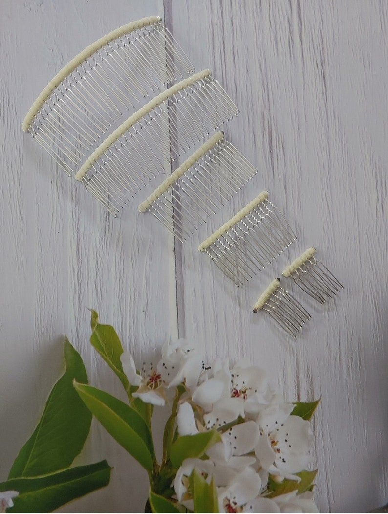 May include: A set of five silver-toned metal hair combs arranged in a descending size order. Each comb features a curved top bar wrapped in a cream-colored fabric. The combs have thin, evenly spaced metal teeth designed for securing hair styles.
