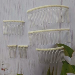 May include: A collection of five silver-toned metal hair combs of varying widths. Each comb features a row of thin, vertical tines attached to a top bar wrapped in a smooth, off-white fabric material. The combs are arranged in different sizes.