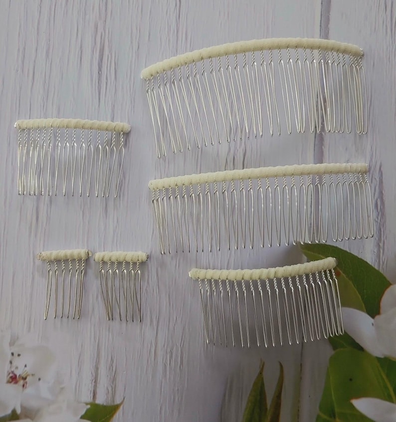 May include: A collection of five silver-toned metal hair combs of varying widths. Each comb features a row of thin, vertical tines attached to a top bar wrapped in a smooth, off-white fabric material. The combs are arranged in different sizes.