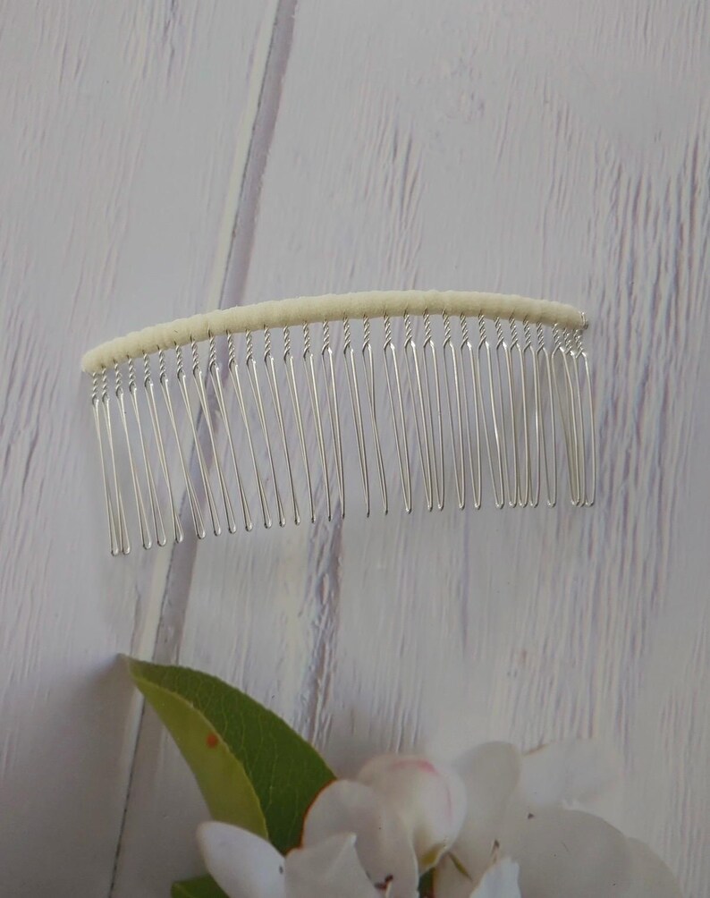 May include: A hair comb featuring a curved, off-white fabric-wrapped top edge and a series of thin, silver-toned metal teeth. The design is simple and functional, with the fabric covering the spine of the comb to provide a clean, finished look.