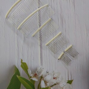 May include: A set of five silver-toned hair combs arranged in a descending size order. Each comb features a curved, off-white fabric-wrapped top edge with multiple thin, parallel metal teeth extending downward for securing hair styles.