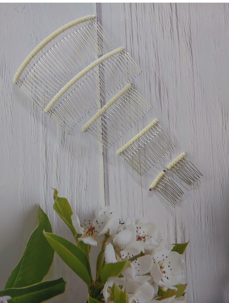 May include: A set of five silver-toned hair combs arranged in a descending size order. Each comb features a curved, off-white fabric-wrapped top edge with multiple thin, parallel metal teeth extending downward for securing hair styles.