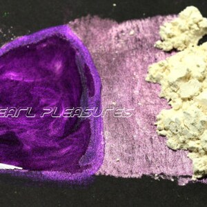 May include: A close-up of a black surface with a vibrant purple liquid and a pile of off-white powder. The text "PEARL PLEASURES" is displayed in white, stylized font across the purple liquid. The powder is textured and granular.