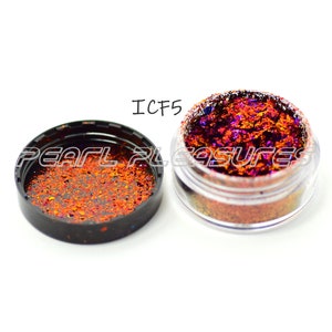 May include: Open clear jar of iridescent glitter with a black lid next to it. The glitter is a mix of orange, purple, and gold flakes. The text "ICF5" is above the jar. The text "PEARL PLEASURES" is on the lid.